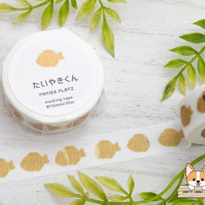 May include: A roll of white washi tape with a brown fish pattern. The tape is labeled "Taiyaki" and "Papier Platz masking tape W15mmx10m".