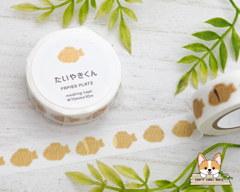 May include: A roll of white washi tape with a brown fish pattern. The tape is labeled "Taiyaki" and "Papier Platz masking tape W15mmx10m".