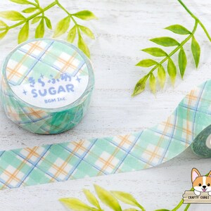 Pode incluir: Um rolo de fita washi com um padr&atilde;o xadrez verde e branco. A fita tem as palavras "Sugar BGM Inc." impressas nela.