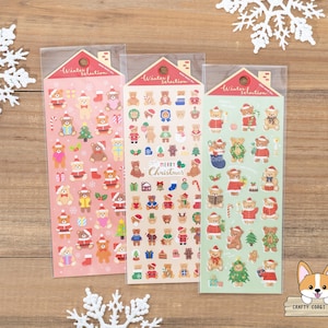 May include: Three sheets of Christmas themed stickers featuring adorable cartoon bears wearing Santa hats, scarves, and other festive attire. The stickers are arranged in a row on a wooden surface. The stickers are perfect for adding a touch of holiday cheer to gifts, cards, and other crafts.
