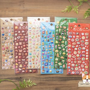 Puede incluir: Cinco hojas verticales de pegatinas pequeñas y coloridas en envases de plástico transparente. Cada hoja presenta un tema distinto que incluye café, productos horneados, aperitivos y comidas, con texto en japonés en la parte superior de cada hoja.