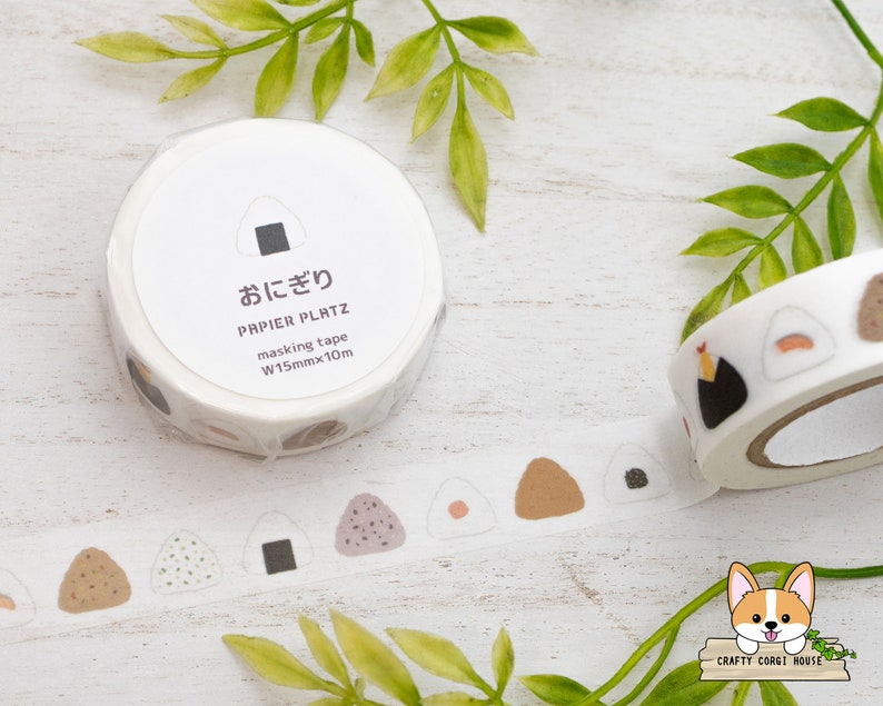 May include: A roll of white washi tape with a repeating pattern of brown, white, and black onigiri (Japanese rice balls). The tape is labeled "おにぎり" (onigiri) and "PAPIER PLATZ masking tape W15mmx10m".