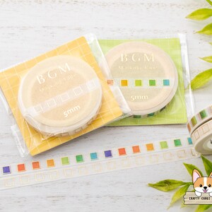 May include: Two rolls of washi tape with a gold and white design. The tape is labeled "BGM Masking Tape" and has a square pattern. The tape is 5mm wide. The tape is on a white wooden surface with green leaves in the background.