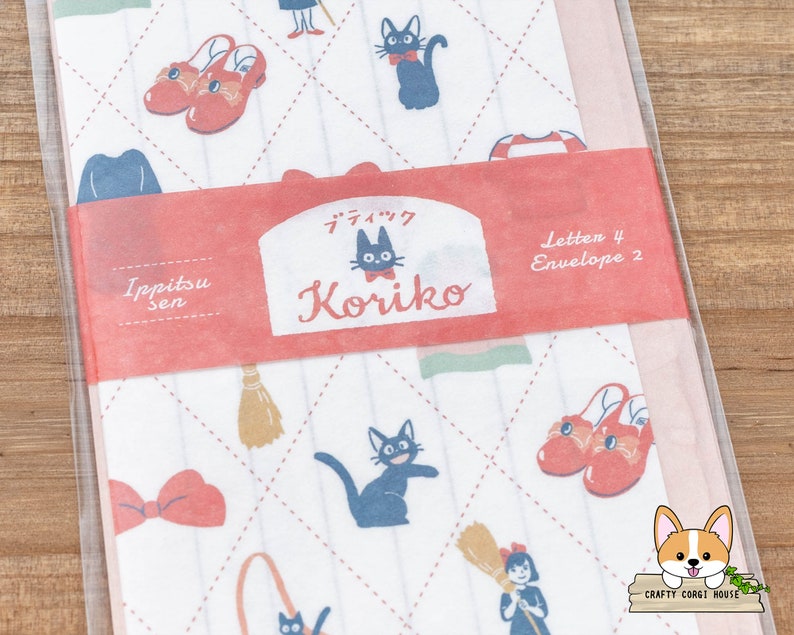 May include: A set of 4 letter writing papers and 2 envelopes featuring a whimsical design with a black cat, red shoes, a broom, and a bow. The paper is white with a pink and green checkered pattern. The text on the paper reads "Ippitsu sen" and "Koriiko".