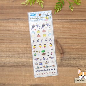 May include: A clear plastic package containing a sheet of colorful stickers with the text "Schedule SEAL". The stickers feature various illustrations of people, pumpkins, and other small objects. The package is on a wooden surface.