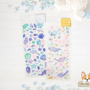 May include: Two sheets of clear sticker paper with colorful sea creature designs. The stickers include dolphins, fish, starfish, and seashells. The text on the sticker sheets reads "Drop Seal".