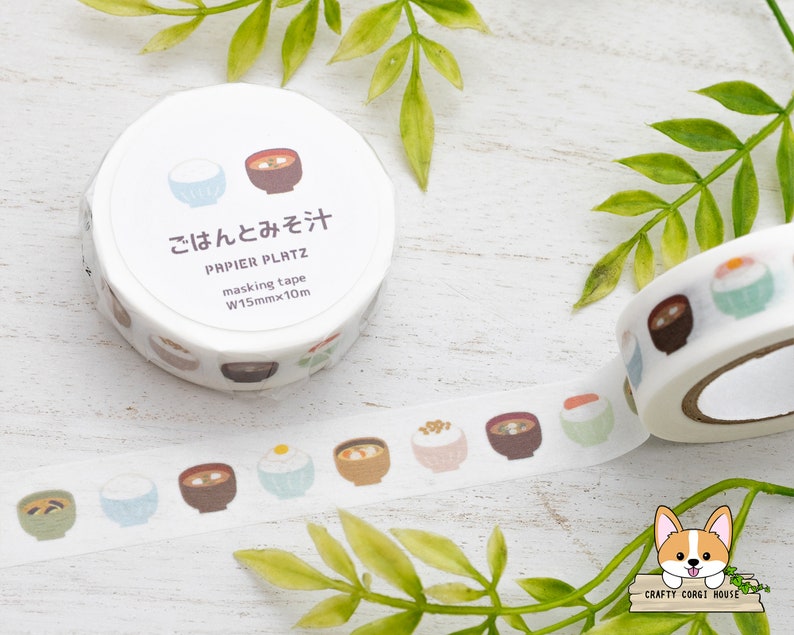 May include: A roll of washi tape with a white background and illustrations of bowls of rice and soup. The tape is labeled "ごはんとみそ汁" and "PAPIER PLATZ masking tape W15mmx10m".