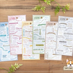 Puede incluir: Una colección de marcadores de papel coloridos con varios diseños de texto y frases. Cada marcador presenta un esquema de color diferente, con palabras como "Precious", "Bright" y "Celestial" impresas en ellos. Los marcadores están dispuestos sobre una superficie de madera.