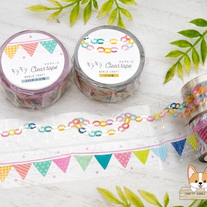 May include: Two rolls of decorative washi tape with colorful designs, including pennants and chain links. The tape rolls are labeled "Clear tape" in Japanese. A roll of tape is unrolled, showing the design. The background is a light wood surface.