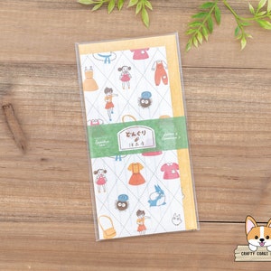 May include: A white and yellow patterned paper with illustrations of a girl wearing a red dress and a black cat. The paper has the text "Letters & Envelopes" and "どんぐり IN.2.2" printed on it.