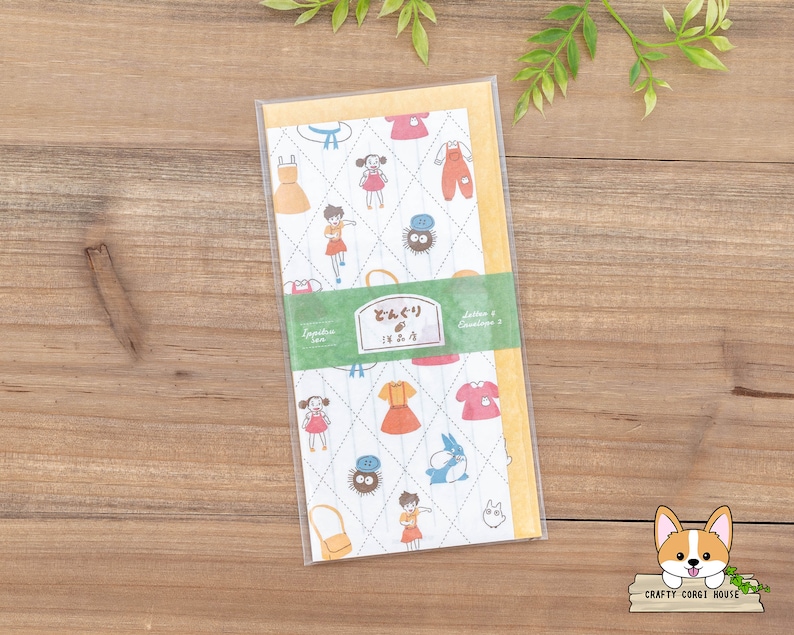 May include: A white and yellow patterned paper with illustrations of a girl wearing a red dress and a black cat. The paper has the text "Letters & Envelopes" and "どんぐり IN.2.2" printed on it.