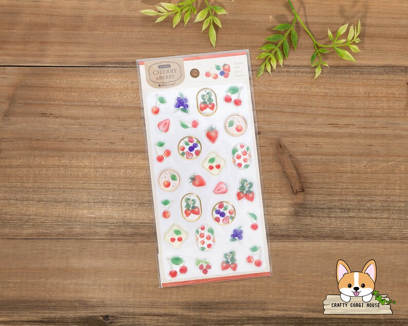 May include: A sheet of clear stickers with a variety of fruit designs, including cherries, strawberries, and blueberries. The stickers are on a white background with a brown border. The text "Cherry & Berry" is printed on the sheet.
