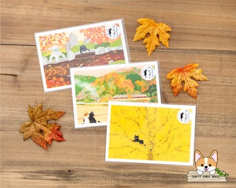 May include: Four illustrated postcards featuring a black cat in different autumnal settings. The postcards are printed on white cardstock and have a clear plastic covering. The cat is depicted in a Japanese garden, a train station, a forest, and a yellow ginkgo tree.