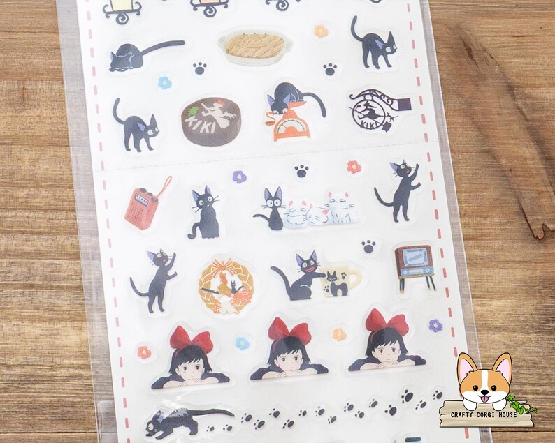 May include: A sheet of stickers featuring illustrations of black cats, a girl with a red bow, and other related imagery. The stickers include various poses of cats, food, and a radio. The stickers are on a white background.