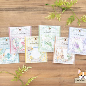 May include: Set of six floral patterned decorative stickers with the word "Ribbloom" printed on each sticker. The stickers are on a wooden surface.
