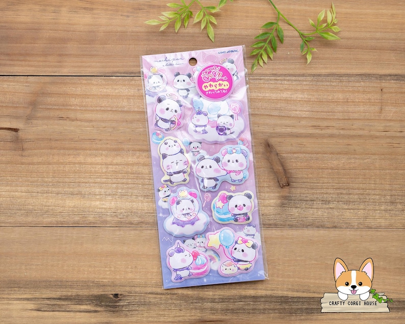 May include: A sheet of stickers featuring cartoon pandas in various poses, some with clouds and balloons. The stickers are in a clear plastic package with Japanese text and a pink logo. The background is a wooden surface.