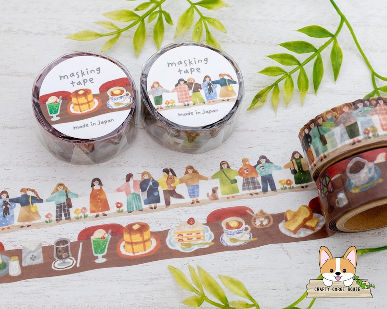 May include: Masking tape rolls with illustrated designs. One roll features people holding hands, the other has food and drink illustrations. The tape is brown with white text that says "masking tape" and "Made in Japan".