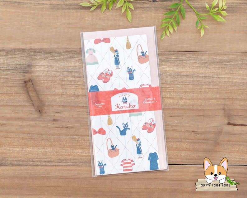May include: A pink and white envelope with a repeating pattern of a black cat, a red shoe, a broom, and a dress. The envelope has the text "Finy Koriiko Letter & Envelope Set" printed on the front.