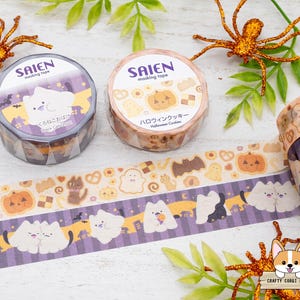 以下が含まれることがあります： ハロウィーンをテーマにしたマスキングテープロール。猫とカボチャのデザイン。テープは紫とオレンジの色使いで、「SAIEN」と日本語のテキストが特徴です。装飾的なクモと葉がテープを囲んでいます。