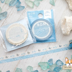 May include: Several rolls of BGM masking tape in shades of blue and white. The tape features wave and whale designs. One package shows the text "FOIL STAMPING" and "5mm". The background includes decorative glass pieces.