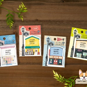 May include: Four colorful shop front stickers with a street lamp and the text "Kotori Machi", which means "Bird Town" in Japanese, and "Shop Side", with a welcome message. The stickers are on a wooden background.
