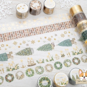 May include: Assortment of gold washi tape rolls with a brick and winter holiday theme. The tape features illustrations of trees, snowflakes, and gold accents. The tape is displayed on a white surface with a snowflake design.
