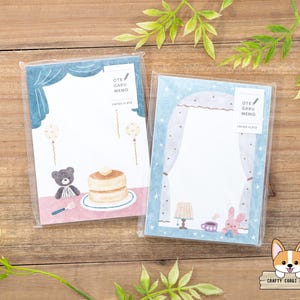 Puede incluir: Dos paquetes de blocs de notas lindos con un diseño azul y blanco. Los blocs de notas presentan un oso con un panqueque y un conejito con una taza de té. Los blocs de notas están etiquetados como "Ote Garu Memo" y "Printed Plate".