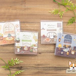 May include: Four packs of "Mattari Animals" stickers are displayed on a wooden surface. Each pack features a different illustrated scene with animals, including a cat, penguin, and other creatures. The packs are in clear plastic.