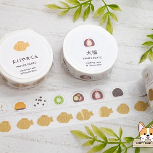 May include: Two rolls of washi tape with Japanese designs. The tape is 1.5 inches wide and 10 meters long. The designs are of a taiyaki (fish-shaped pastry) and a mochi (Japanese rice cake).