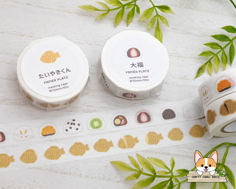 May include: Two rolls of washi tape with Japanese designs. The tape is 1.5 inches wide and 10 meters long. The designs are of a taiyaki (fish-shaped pastry) and a mochi (Japanese rice cake).