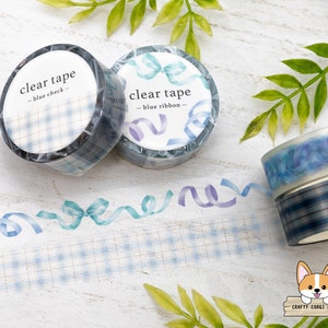 Puede incluir: Dos rollos de cinta transparente con patrones de cuadros azules y blancos y diseños de cinta azul. El texto en la cinta dice "clear tape - blue check" y "clear tape - blue ribbon".