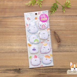 May include: A sheet of stickers featuring cartoon characters resembling mochi desserts. Each sticker has a white base with colorful fruit-themed accents, such as strawberries, oranges, and grapes. The stickers are packaged on a clear backing with Japanese text and a pink circular sticker.
