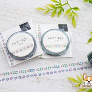May include: Two rolls of clear tape with floral designs are displayed. Each roll is packaged in a clear plastic wrapper. The tape rolls are labeled "clear tape - stitch" and are 7 mm wide. A length of decorative tape with a floral pattern is also visible.