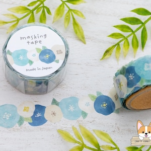 May include: A roll of masking tape with a floral design in shades of blue and white. The tape is in a clear plastic container with the words "masking tape" and "made in Japan" printed on it. The tape is unrolled, showing the floral pattern.