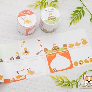 Puede incluir: Un conjunto de rollos de cinta washi con temática japonesa. Los rollos presentan ilustraciones de perros, bollos y otros alimentos. El texto en los rollos dice "Roll付" y "Papier Platz".