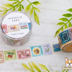 May include: A roll of masking tape with a stamp design. The tape is in a clear plastic container with the words "masking tape" and "Made in Japan". The tape features colorful stamp illustrations of flowers, fruit, and animals.