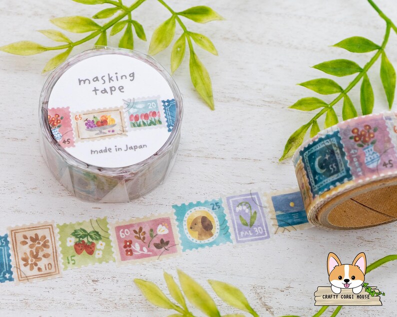May include: A roll of masking tape with a stamp design. The tape is in a clear plastic container with the words "masking tape" and "Made in Japan". The tape features colorful stamp illustrations of flowers, fruit, and animals.