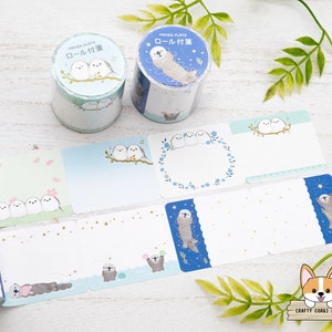 Puede incluir: Un conjunto de rollos de cinta washi decorativos en un esquema de color azul y blanco. Los rollos presentan ilustraciones de pájaros y nutrias marinas. El texto en los rollos dice "Paper Platz" y "Roll Tape".