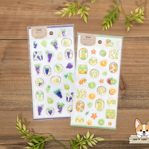 May include: Two sheets of stickers featuring fruit designs. The first sheet has a grape theme with purple grapes and green leaves. The second sheet has a kiwi fruit theme with green kiwi fruit and yellow stars. Both sheets have the text "Crafty Corgi House" on the bottom.