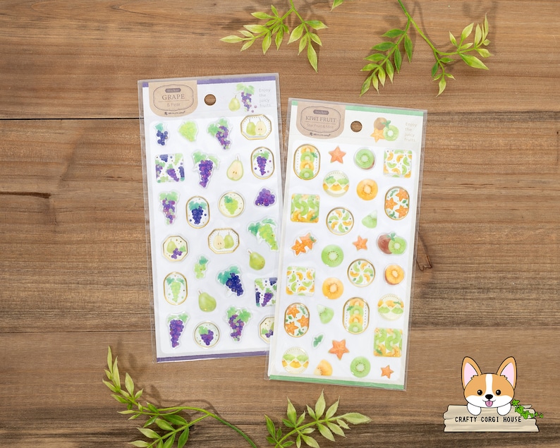 May include: Two sheets of stickers featuring fruit designs. The first sheet has a grape theme with purple grapes and green leaves. The second sheet has a kiwi fruit theme with green kiwi fruit and yellow stars. Both sheets have the text "Crafty Corgi House" on the bottom.