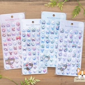 Peut inclure: Quatre feuilles d'autocollants alphabet irisés sur le thème des ballons. Chaque feuille présente un schéma de couleurs différent de rose, bleu et violet.