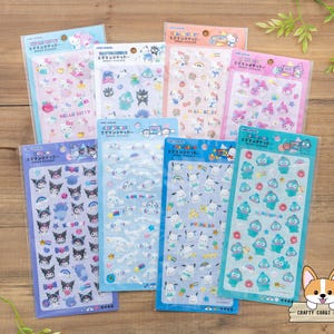 May include: A collection of colorful sticker sheets featuring various cartoon characters. The sheets are packaged in clear plastic and arranged on a wooden surface. The stickers have different colors and designs, including Hello Kitty and other popular characters.