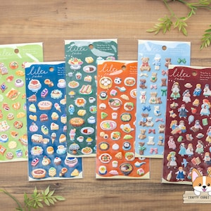 May include: Six vertical sticker sheets labeled lilte, featuring various designs including pastries, cakes, tea sets, teddy bears, and small figures in dresses. The sheets are arranged in a row, each with a different background color: green, blue, dark green, orange, light blue, and maroon.