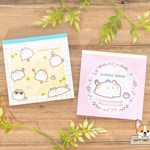 May include: Two pink and yellow memo pads with a cute cartoon cat design. The memo pads feature the text "Zundo-Neko" and a small mouse character.
