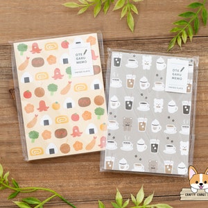 May include: Two packs of memo paper with cute illustrations. One pack features a brown and white coffee cup pattern with bears and other animals. The other pack features a yellow background with a variety of Japanese food illustrations. Both packs have the text "OTE GARU MEMO PAPER PLATZ" on them.