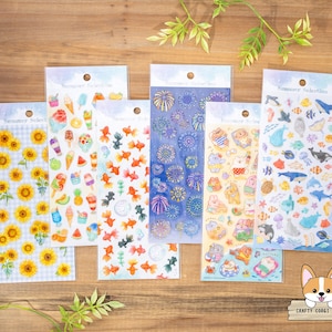 Op de afbeelding: Een verzameling stickerbladen met zomerthema's. De stickers bevatten zonnebloemen, ijs, goudvissen, vuurwerk en zeeleven. Elke vel is verpakt in een transparante plastic hoes.