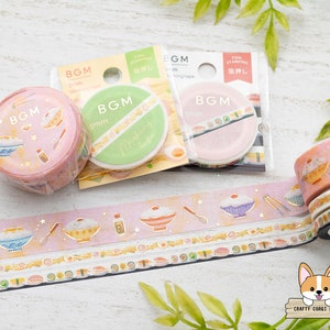 May include: Assortment of washi tapes featuring a Japanese food theme. The tapes are pink, yellow, and white with illustrations of bowls of rice, sushi, and other Japanese food. The tapes are 5mm wide and are labeled "BGM".