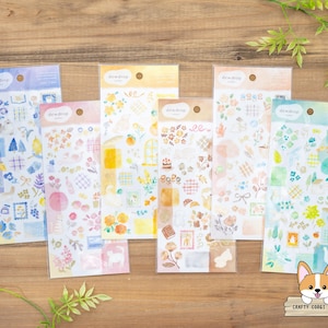 Pode incluir: Uma coleção de folhas de autocolantes com vários desenhos, incluindo padrões florais, chávenas de chá e elementos arquitetónicos. Os autocolantes são em cores pastel, com o nome da marca "dewdrop" impresso no topo de cada folha. O logótipo Crafty Corgi House está em baixo.