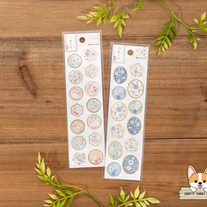 以下が含まれることがあります： 花柄と鳥のデザインの装飾用ステッカーが2枚セットになっています。ステッカーは白い背景に金色のアクセントが施されています。ステッカーは透明なプラスチックの包装に入っています。