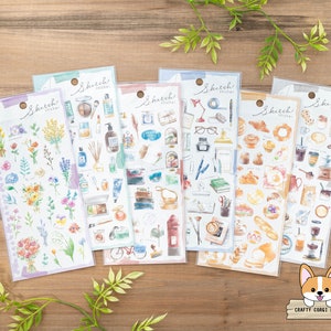 May include: Set of six sheets of watercolor stickers featuring various themes. The first sheet features floral designs in shades of pink, purple, and blue. The second sheet features beauty and cosmetic items in shades of pink, blue, and green. The third sheet features a variety of objects in shades of blue, green, and brown. The fourth sheet features office supplies in shades of blue, green, and brown. The fifth sheet features bakery items in shades of brown, yellow, and white. The sixth sheet features coffee and tea items in shades of brown, white, and black.